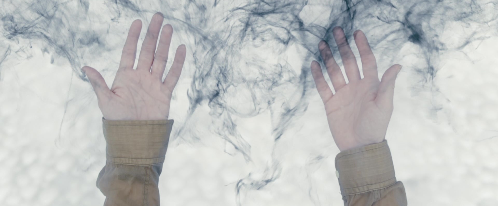 Two upraised hands pressed against a misty white barrier, with dark inky tendrils swirling around them.