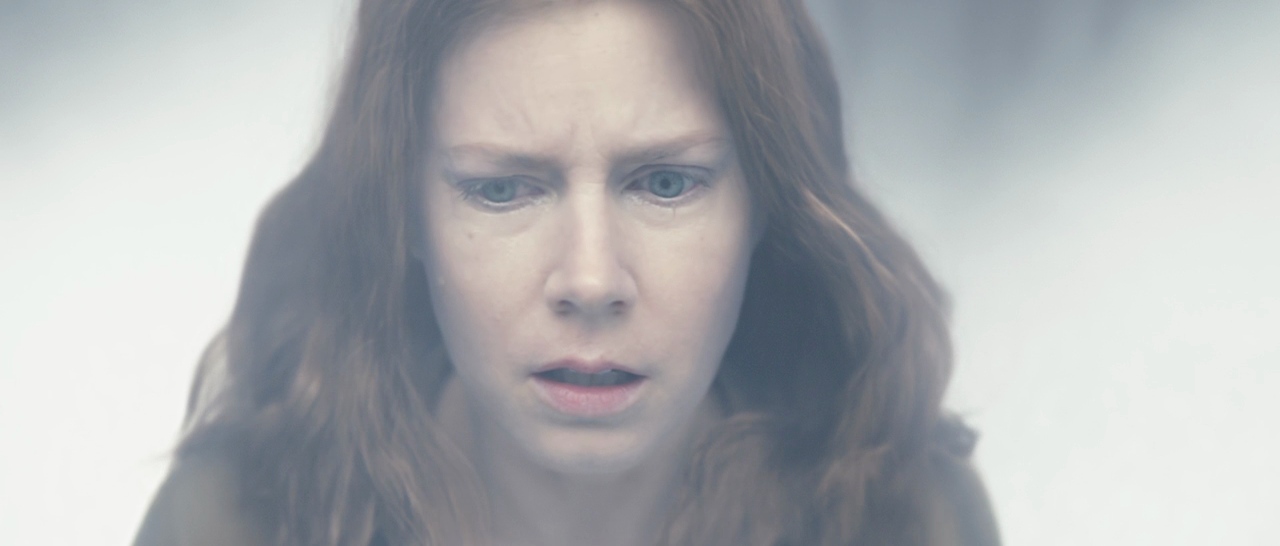 A close-up of a red-haired woman looking down with a troubled, tearful expression against a pale white background.