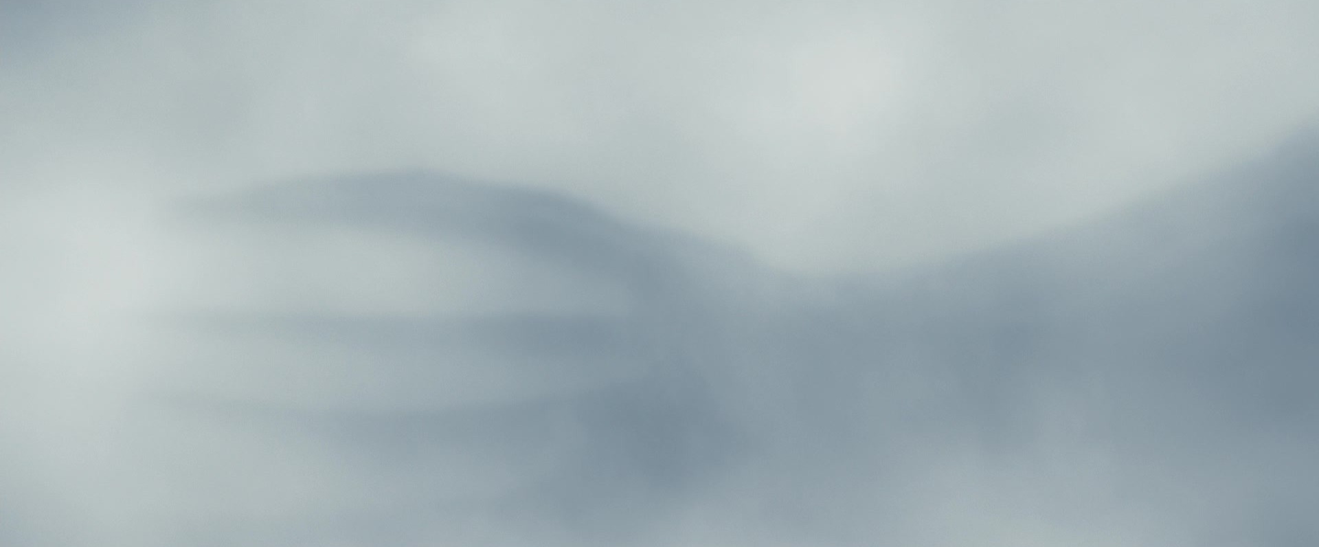 A blurred grey close-up of a huge seven-fingered alien hand pressing against mist.