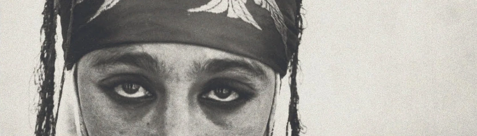 A close-up crop of a black-and-white photograph, framed tightly on a woman's eyes and the top of her headscarf.